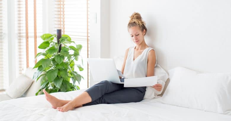 Mulher trabalhando no laptop e sentado na cama em casa | 5 Dicas Para Decorar o Quarto Com Plantas
